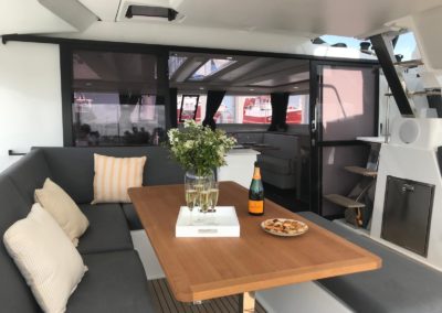 Cockpit du Tanna 47 avec sol en teck synthétique, grande table convivial en bois exotique. Nombreuses assises avec coussins ey grand rangement dans les assises. Concept Open avec une belle circulation entre le cockpit et le carré. Frigo de cockpit. Enceinte extérieur Fusion connecté au poste Fusion. Accès vers le poste de barre et le skylounge sur le roof.