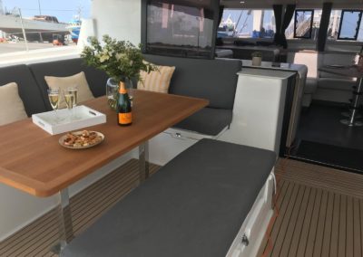 Cockpit du Tanna 47 avec sol en teck synthétique, grande table convivial en bois exotique. Nombreuses assises avec coussins ey grand rangement dans les assises. Concept Open avec une belle circulation entre le cockpit et le carré.