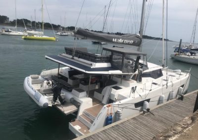 Fountaine Pajot Tanna 47 amarré sur un ras de quai en bretagne. Panneaux solaires sur l'arrière du Roof. Annexe Gala avec son moteur Suzuki sur une plateforme de bain hydraulique. Cockpit en Teck synthétique avec plancha intégré.