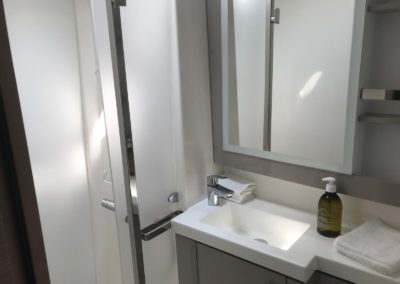 Une des salles de bain du Tanna 47 avec lavabo, miroir, nombreux rangements et douche séparé d'une paroi.